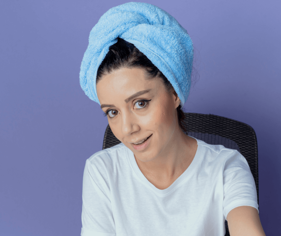 smiling young pretty girl sitting makeup table with makeup tools with bath towel head looking camera isolated purple background