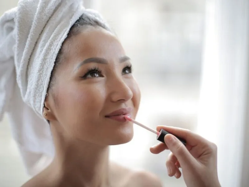 Woman applying a glossy tinted lip oil with a doe-foot applicator