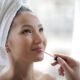 Woman applying a glossy tinted lip oil with a doe-foot applicator