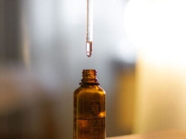 A dropper of serum over an amber glass bottle