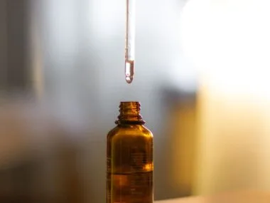 A dropper of serum over an amber glass bottle