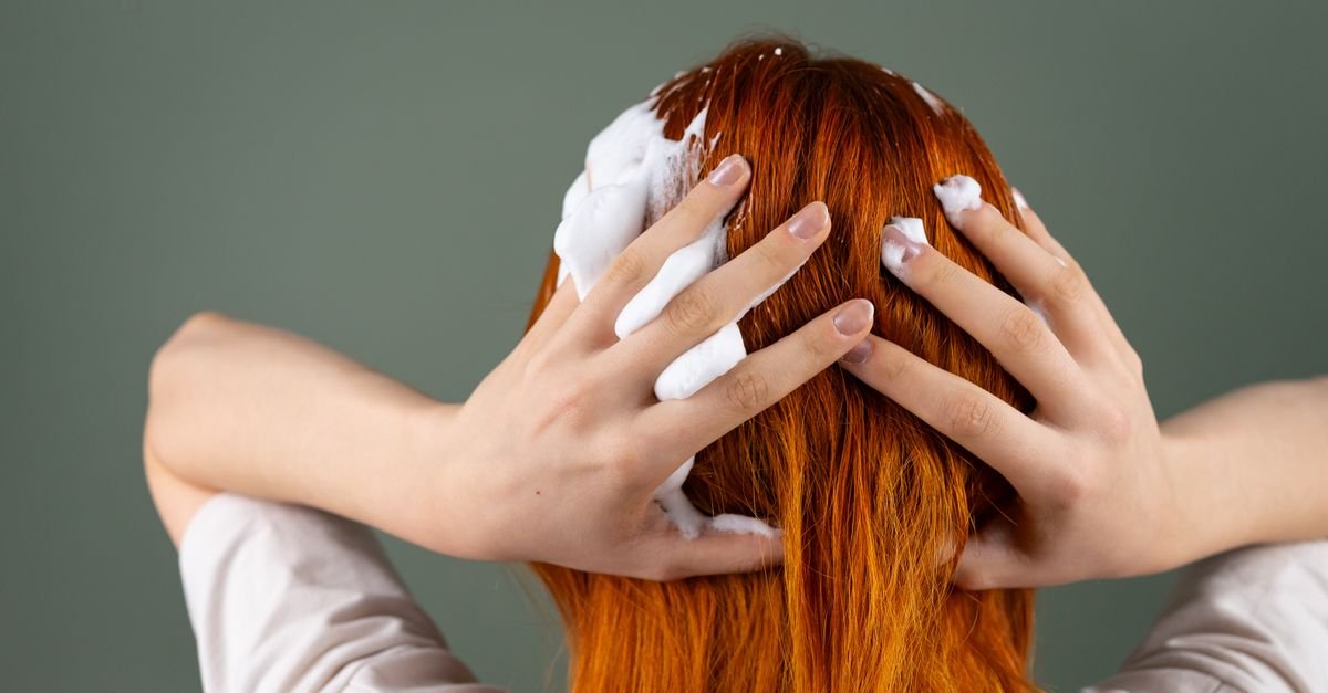 Hands lathering shampoo through red hair