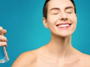 A smiling woman misting her face with a spray bottle