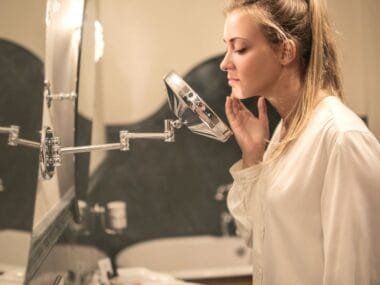 A woman examining her face closely at a bathroom mirror
