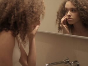 A woman examining her skin closely in the bathroom mirror