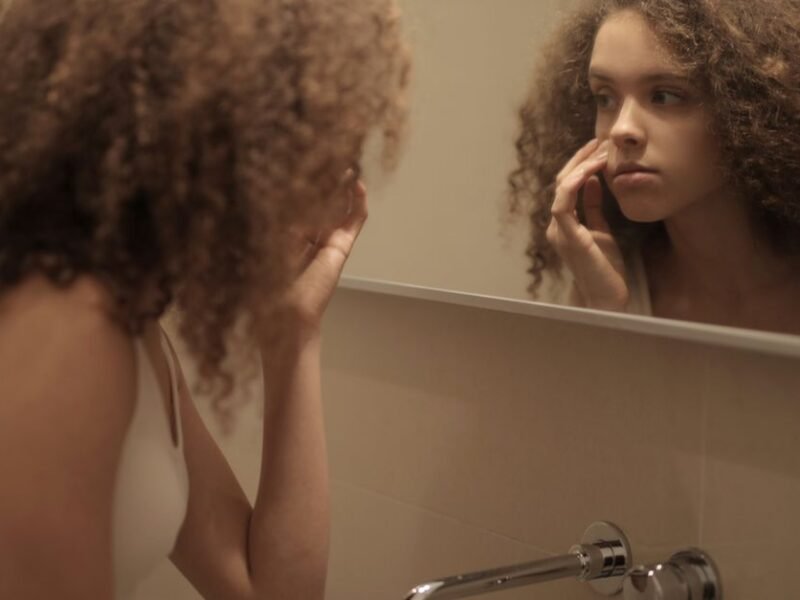 A woman examining her skin closely in the bathroom mirror