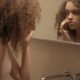 A woman examining her skin closely in a bathroom mirror