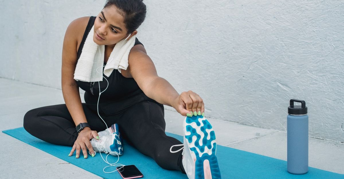 A woman stretching at the gym beside a water bottle