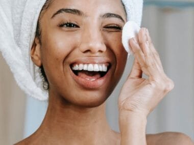 A woman with a towel wrap holding a cotton pad, laughing