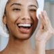 A woman with a towel wrap holding a cotton pad, laughing