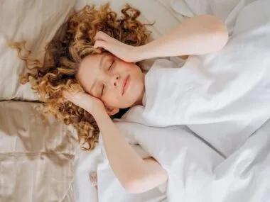 A woman lying in bed touching her forehead in the morning