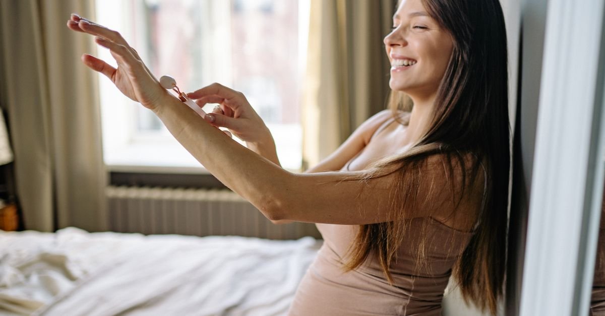 A smiling woman applying lotion by a bright window
