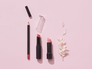 A flat lay of lipsticks and makeup pencils on pink