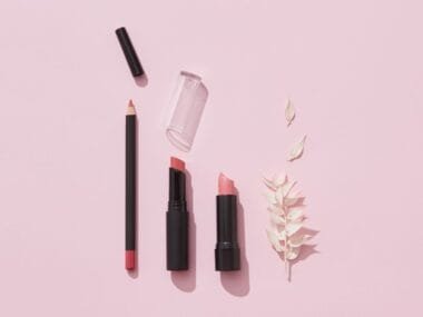 A flat lay of lipsticks and makeup pencils on pink