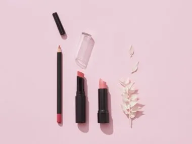 A flat lay of lipsticks and makeup pencils on pink