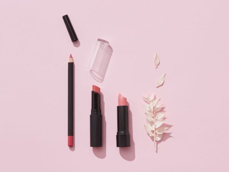 A flat lay of lipsticks and makeup pencils on pink