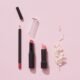 A flat lay of lipsticks and makeup pencils on pink