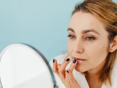 A woman applying lip balm at a mirror