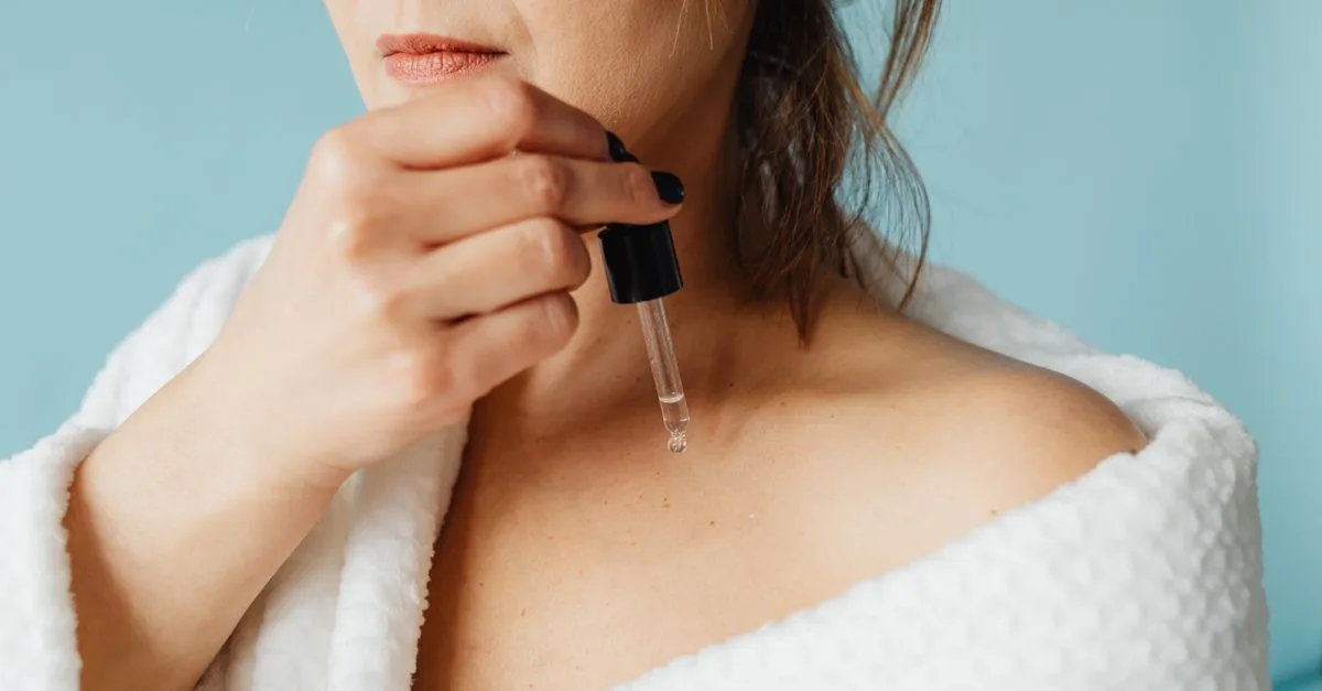 A woman in a robe applying serum to her face