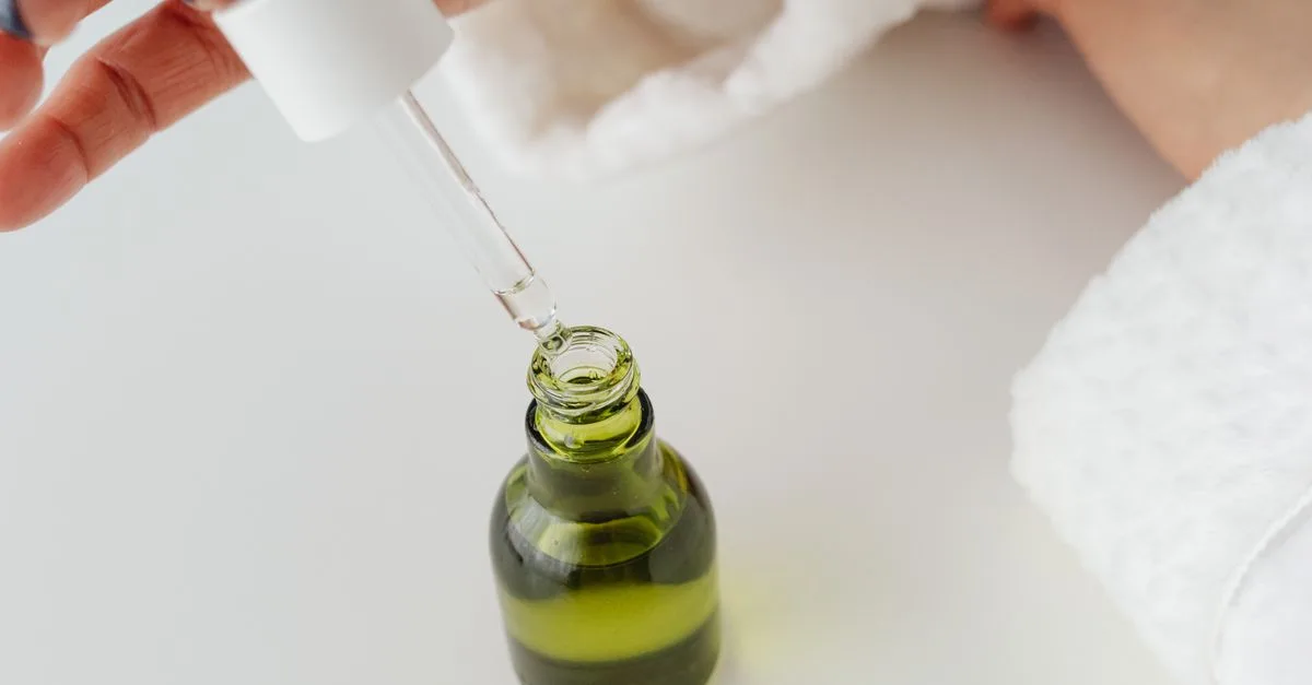 A dropper drawing oil from a green glass bottle
