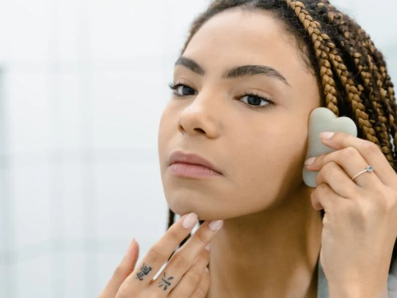 A woman using a gua sha stone on her cheek