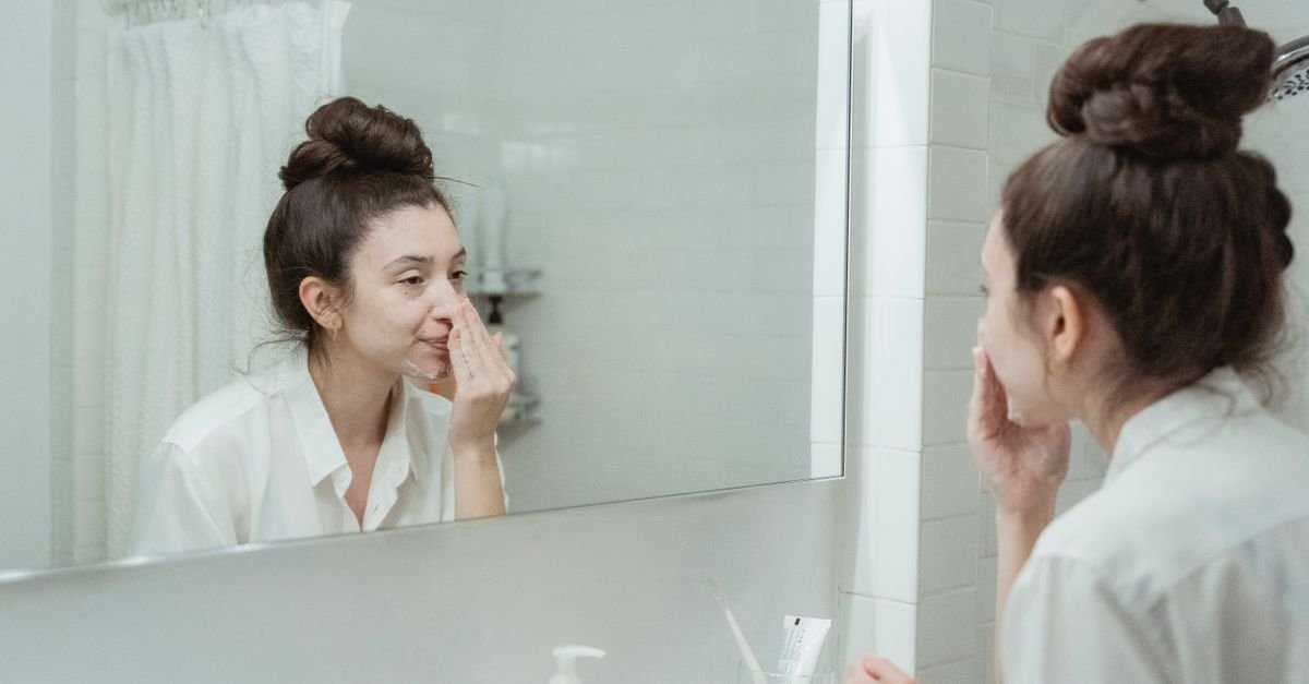 A woman examining her skin in a bathroom mirror