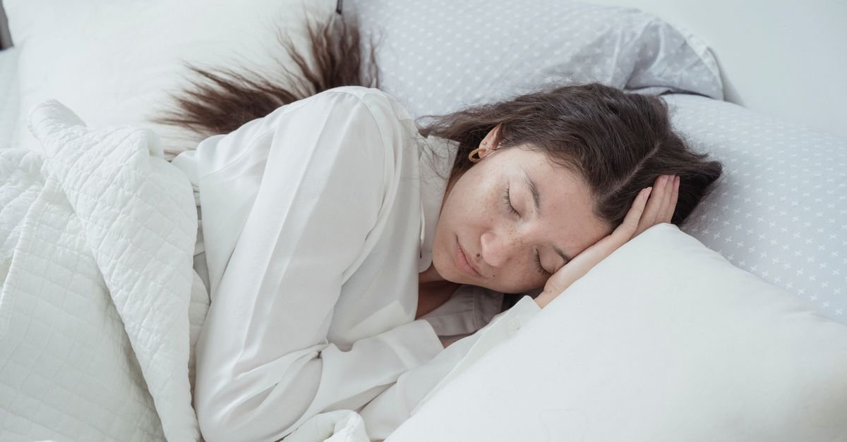 A woman sleeping on her side on white bedding