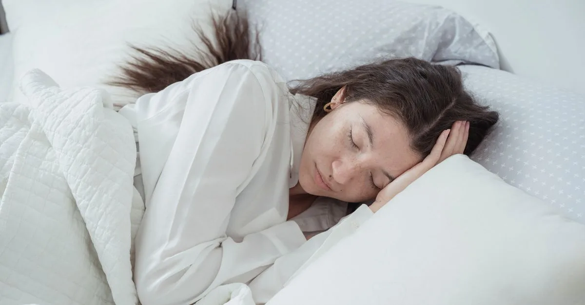 A woman sleeping on her side on white bedding