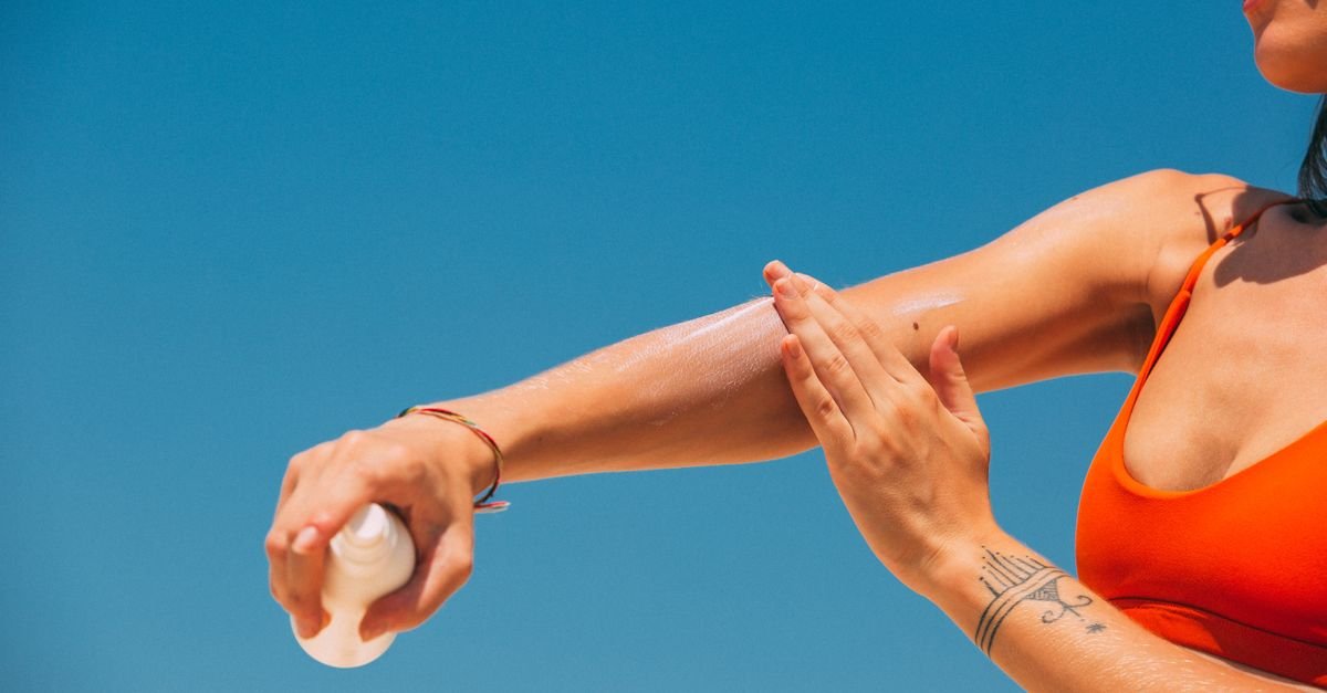 A woman applying sunscreen to her arm under a blue sky