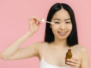A smiling woman applying facial oil with a dropper