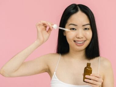 A smiling woman applying facial oil with a dropper