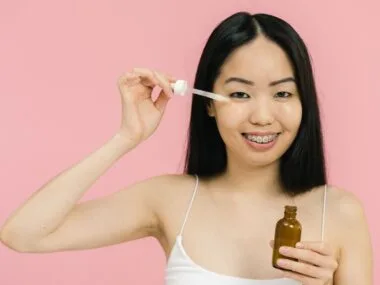A smiling woman applying facial oil with a dropper