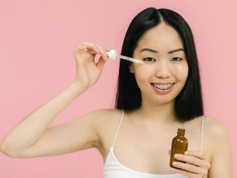 A smiling woman applying facial oil with a dropper