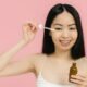 A smiling woman applying facial oil with a dropper