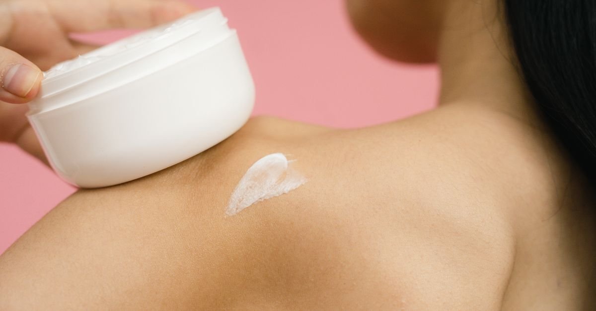 Cream applied to a bare shoulder from an open jar