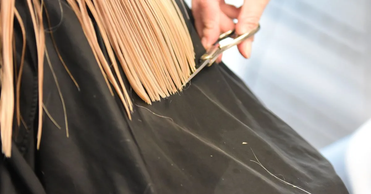 A hairdresser trimming hair ends over a cape