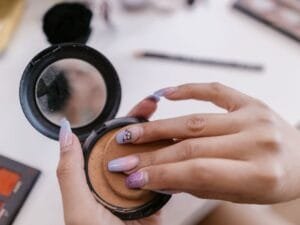 A hand opening a pressed powder compact over a makeup table