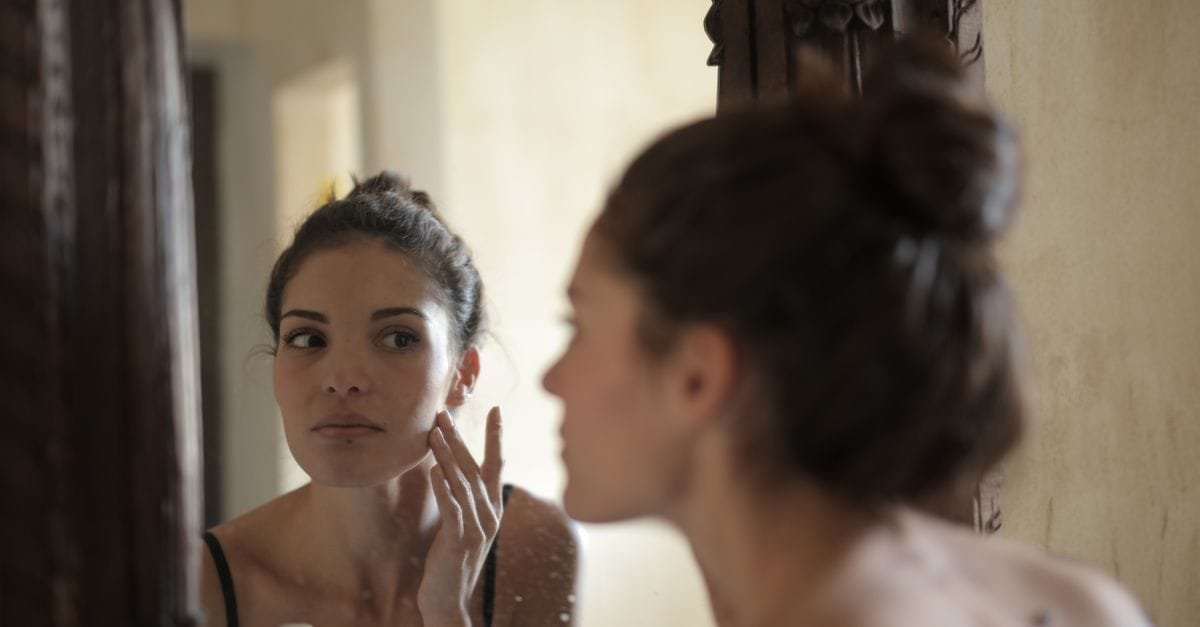 A woman inspecting her skin at a mirror