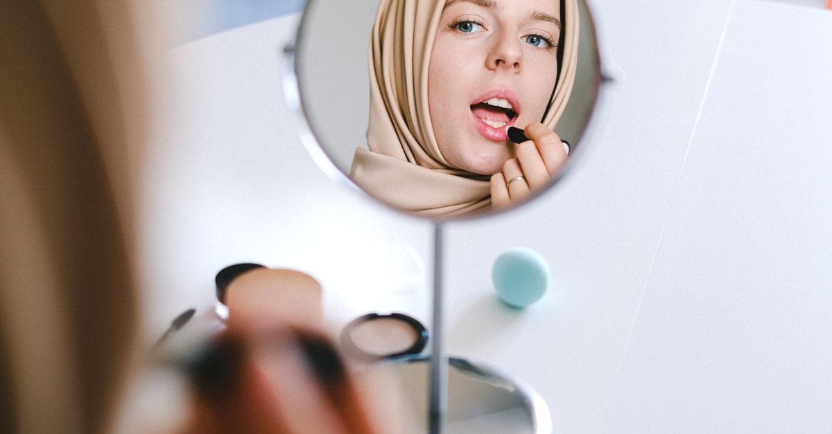 A woman applying makeup at a small round mirror