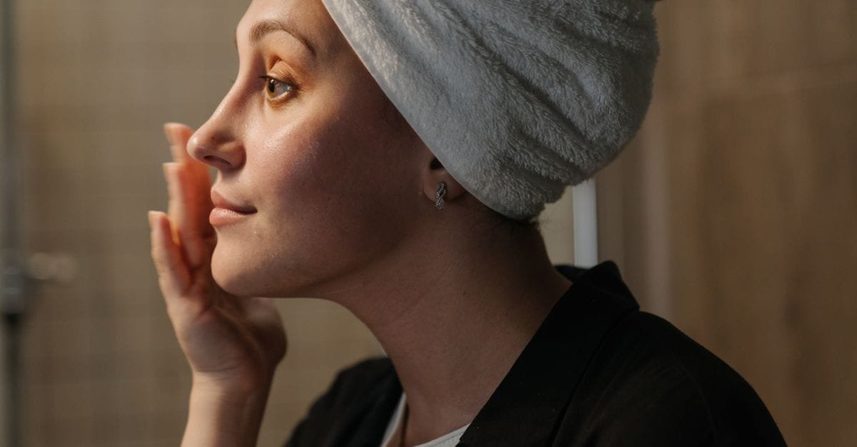 A woman with a towel wrap applying skincare