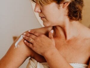 A woman applying lotion to her shoulder after a shower