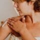 A woman applying lotion to her shoulder after a shower