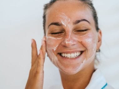 A smiling woman with moisturizer dabs on her face