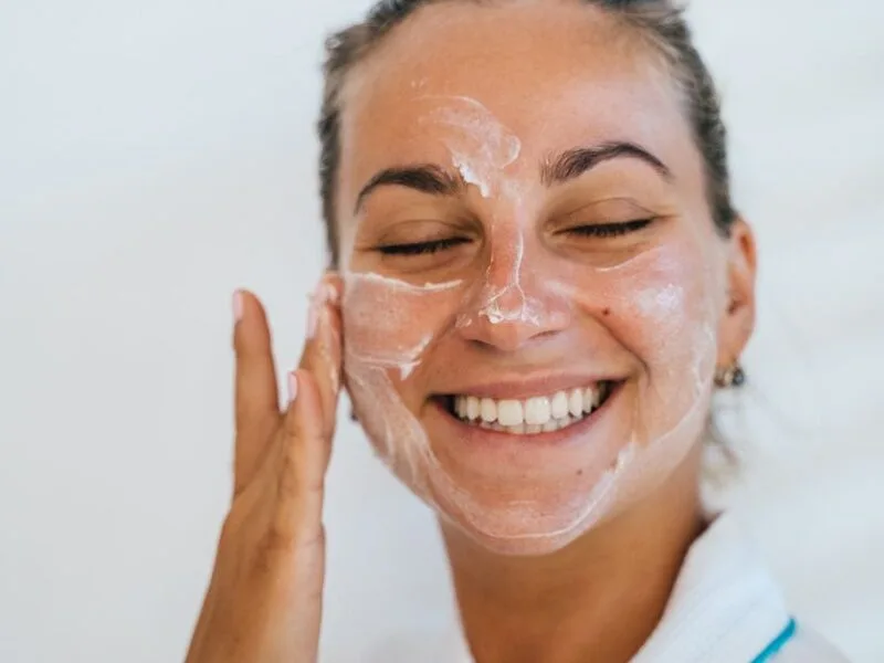 A smiling woman with moisturizer dabs on her face