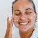 A smiling woman with moisturizer dabs on her face