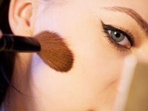 A brush applying blush to a cheek in close-up