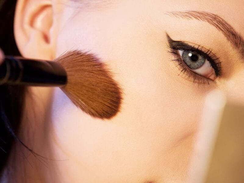 A brush applying blush to a cheek in close-up