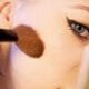 A brush applying blush to a cheek in close-up