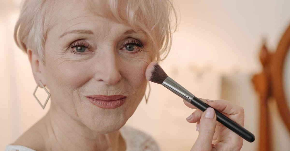 A mature woman smiling while applying makeup