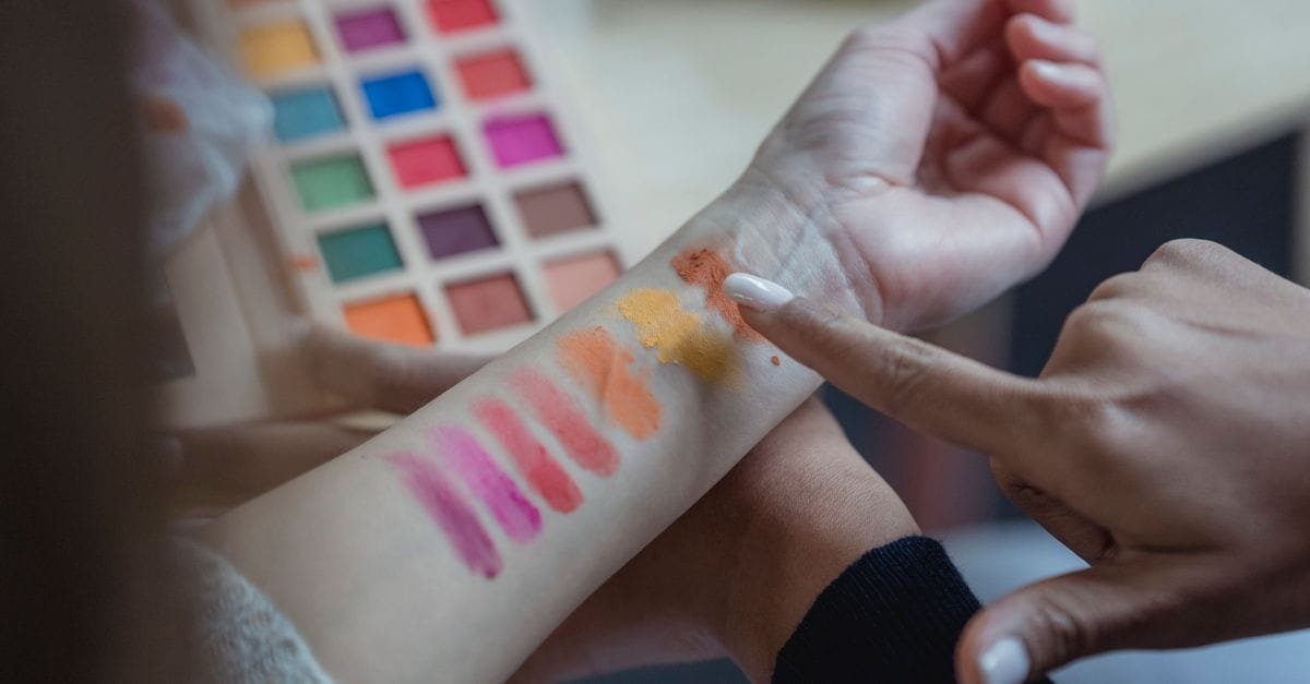 Colorful makeup swatches on an arm beside a palette